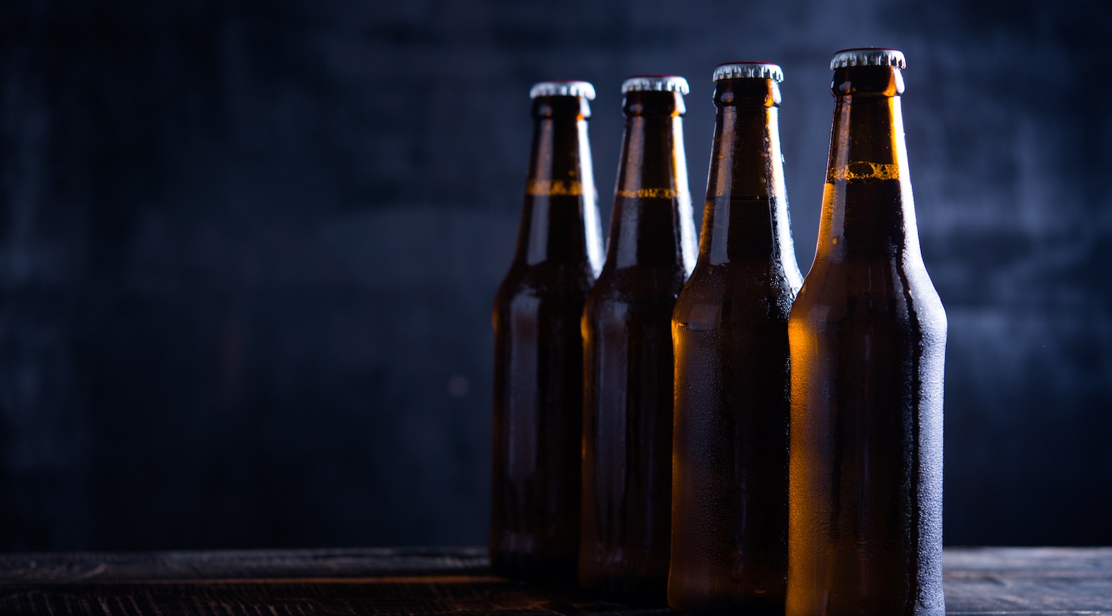 Glass bottles of beer with glass and ice on dark background